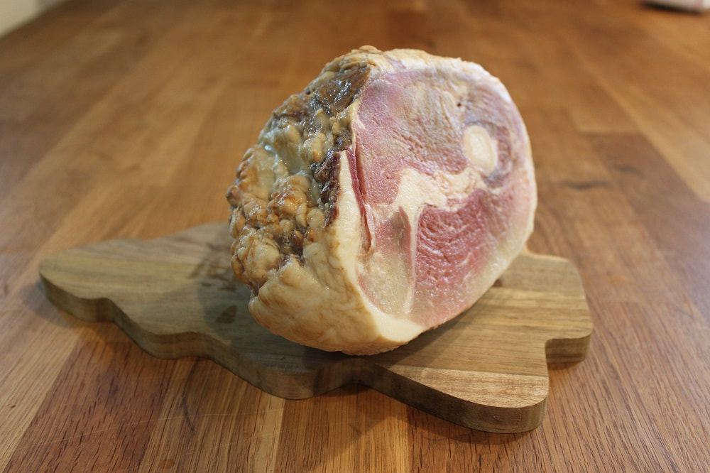 An nice piece of uncooked pastured pork roast set on a pine tree shaped cutting board.